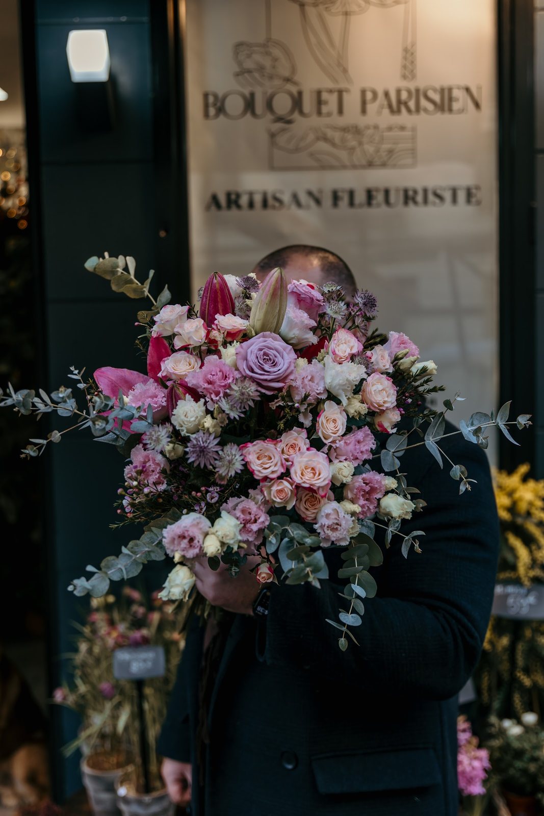 Grand bouquet de roses, lisianthus et eucalyptus devant l’affiche de la boutique